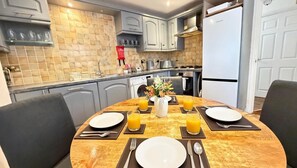 A dining area with a marble table set for two, a vase with flowers, and two glasses of orange juice. - Spacious Townhouse central Leamington with parking (Royal Leamington Spa)
