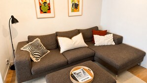 Ein braunes Ecksofa mit drei Kissen, ein kleiner Holztisch mit Tablett und zwei gerahmte Kunstwerke an der Wand.