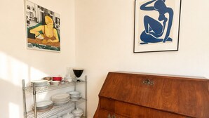 Ein Zimmer mit einem Holzschrank, einem Metallregal mit Geschirr und zwei gerahmten Kunstwerken an der Wand.