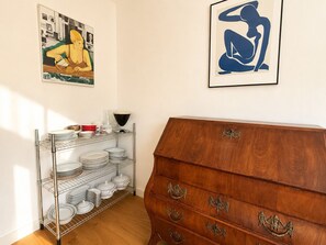 Ein Zimmer mit einem Holzschrank, einem Metallregal mit Geschirr und zwei gerahmten Kunstwerken an der Wand.