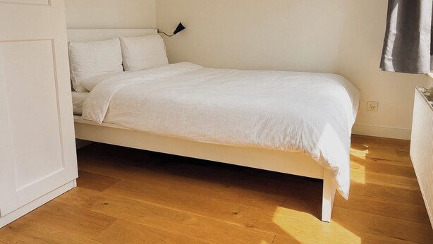Ein Zimmer mit einem Einzelbett, Holzboden, weißen Wänden und einer weißen Bettdecke.