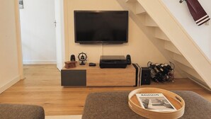 Ein Wohnzimmer mit einem an der Wand befestigten Flachbildfernseher, einer Holz-Unterhaltungsecke, einer Treppe und einer Zeitschrift auf einem Tablett.