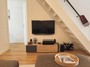 Ein Wohnzimmer mit einem an der Wand befestigten Flachbildfernseher, einer Holz-Unterhaltungsecke, einer Treppe und einer Zeitschrift auf einem Tablett.