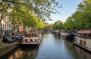 A canal lined with boats, narrow buildings, and trees. - Welcome home (Amsterdam)