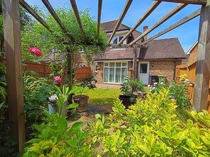 A garden with a wooden pergola, potted plants, and a brick house with a window. - Luxury & Spacious Refurbished 3-Bed Guildford Home with Garden & London Links (Guildford)
