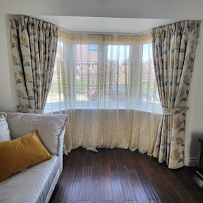 A room with a bay window, a sofa with a mustard-colored pillow, and a patterned curtain. - Luxury & Spacious Refurbished 3-Bed Guildford Home with Garden & London Links (Guildford)
