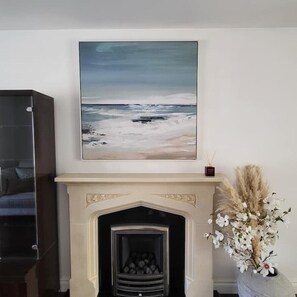 A fireplace with a mantel, a framed painting above it, and a vase with flowers to the right. - Luxury & Spacious Refurbished 3-Bed Guildford Home with Garden & London Links (Guildford)