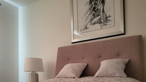 Siististi pedattu sänky, jossa on kuviollinen päiväpeite ja kaksi tyynyä, yöpöydällä oleva lamppu ja seinällä oleva kehystetty taideteos.