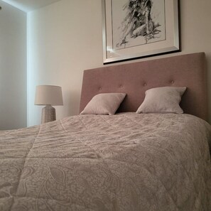A neatly made bed with a patterned bedspread and two pillows, a bedside lamp, and a framed artwork on the wall. - Luxury & Spacious Refurbished 3-Bed Guildford Home with Garden & London Links (Guildford)