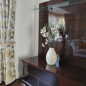 A room with a dark wooden cabinet, a glass shelf, and a white vase with white flowers. - Luxury & Spacious Refurbished 3-Bed Guildford Home with Garden & London Links (Guildford)