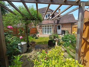 A garden with a wooden pergola, potted plants, and a brick house in the background. - Luxury & Spacious Refurbished 3-Bed Guildford Home with Garden & London Links (Guildford)