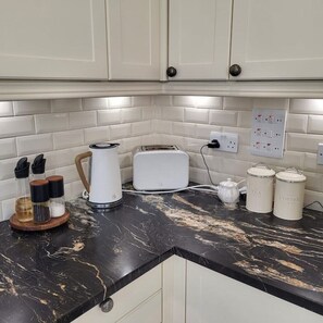 A kitchen with white cabinets, a marble countertop, a kettle, a toaster, and two containers labeled 'TEA' and 'COFFEE'. - Luxury & Spacious Refurbished 3-Bed Guildford Home with Garden & London Links (Guildford)