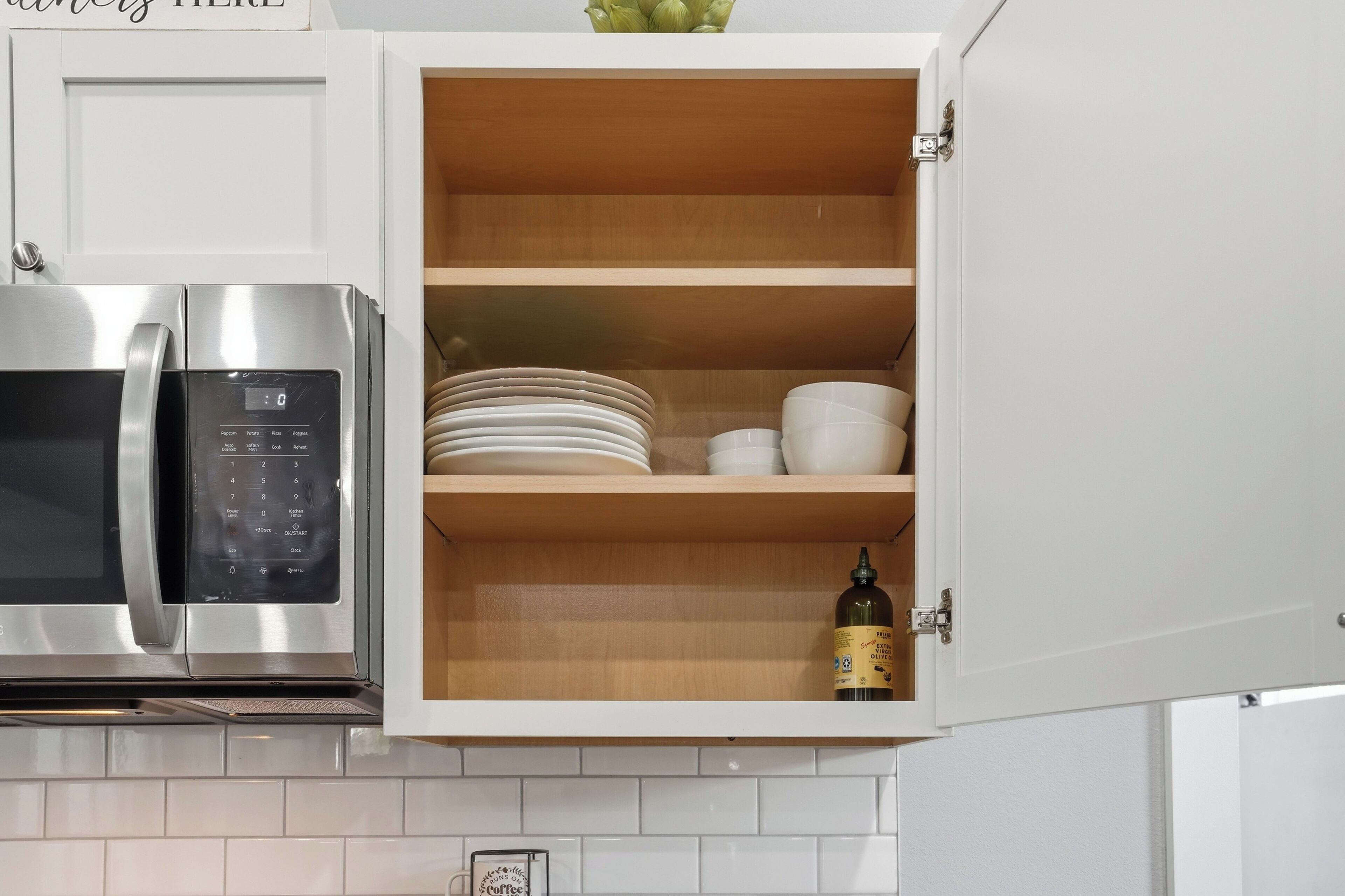 A kitchen with a built-in microwave, a stainless steel refrigerator, and a wooden cabinet with dishes and a bottle.