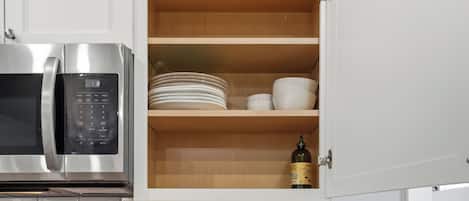 A kitchen with a built-in microwave, a stainless steel refrigerator, and a wooden cabinet with dishes and a bottle.