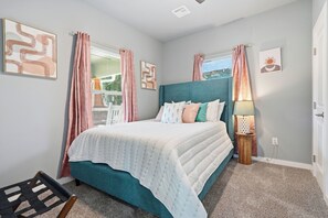 A bedroom with a bed, a bedside table with a lamp, a chair, and a window with curtains. - Modern Retreat in Downtown Tulsa: Sleeps 7 (Tulsa)