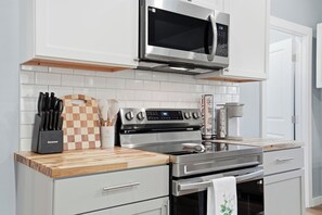 A modern kitchen with stainless steel appliances, a wooden countertop, and a checkered cutting board. - Modern Retreat in Downtown Tulsa: Sleeps 7 (Tulsa)