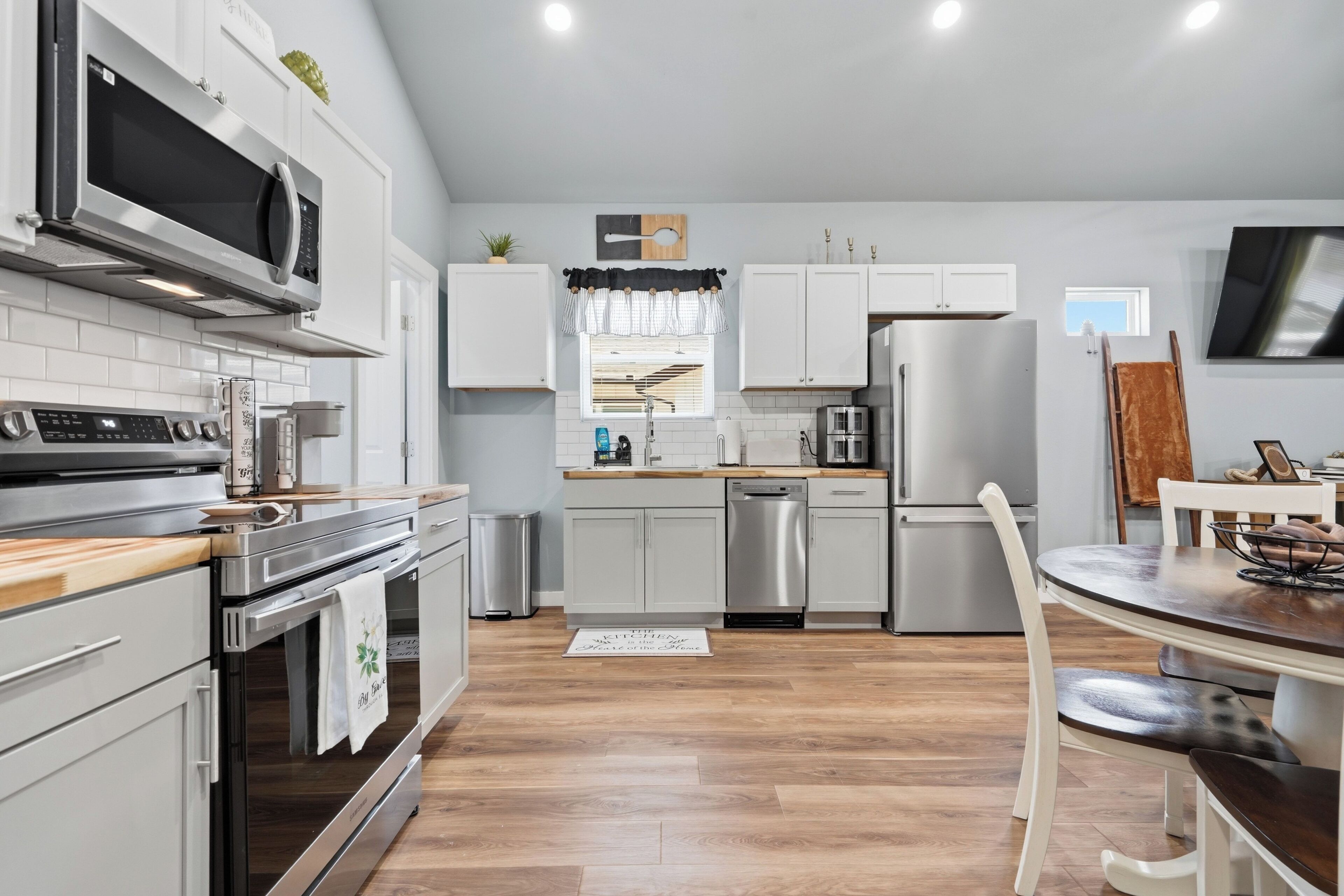 A modern kitchen with stainless steel appliances, white cabinetry, and a wooden dining table.