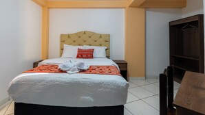 Habitación de hotel con cama, mesita de noche, armario de madera y suelo de baldosas.