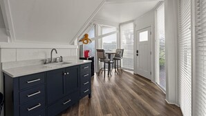 A modern kitchen with dark cabinets, a white countertop, and a dining area with two chairs and a table.