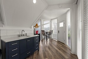 Una cocina moderna con armarios oscuros, una encimera blanca y una zona de comedor con dos sillas y una mesa.