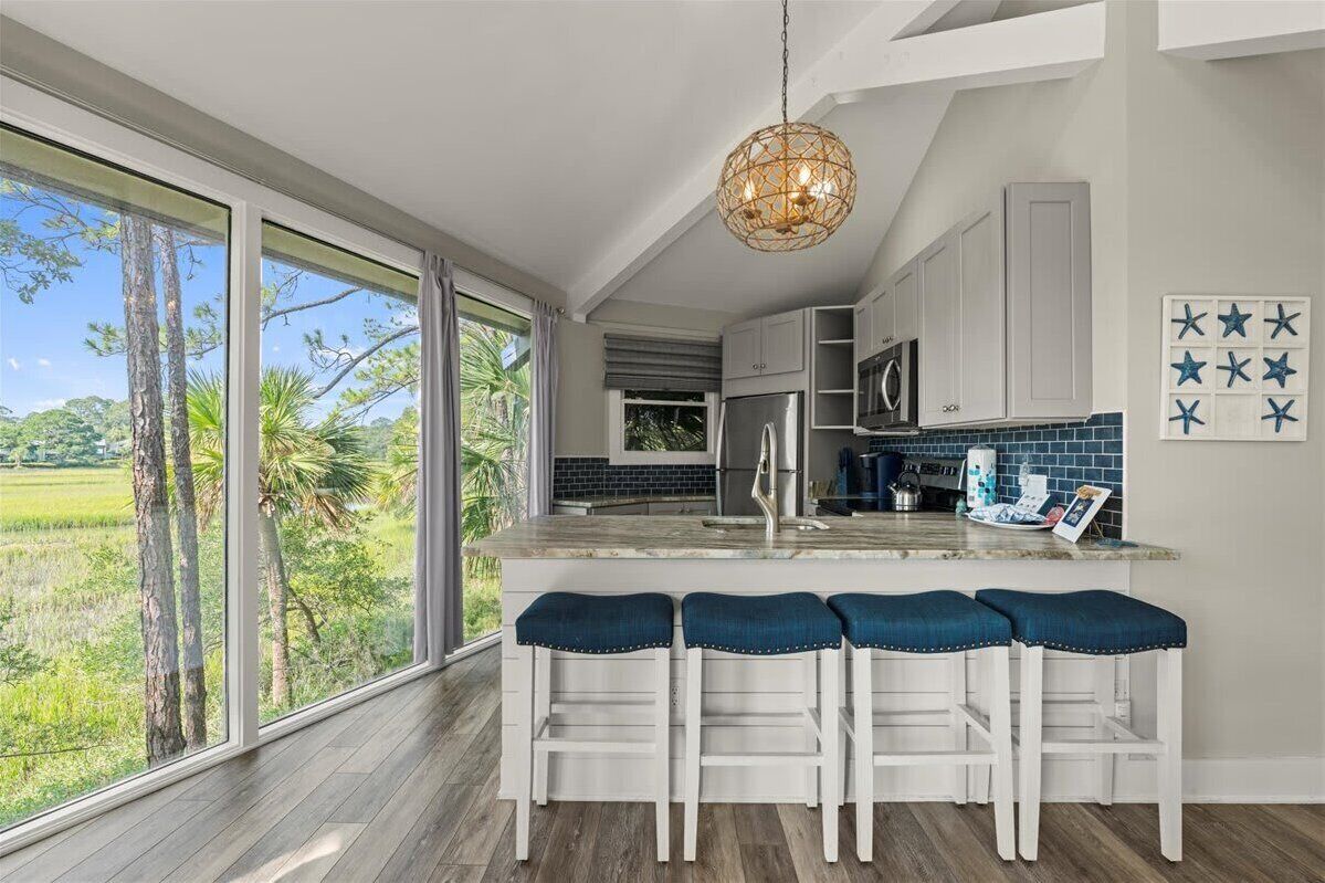 A modern kitchen with a large island, white cabinets, and a view of a green landscape.