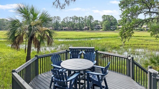 A wooden deck with a round table and chairs overlooking a rice field.
