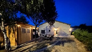 Un edificio de dos pisos con suelo de tierra, una estructura de madera a la izquierda y un patio con mobiliario exterior.