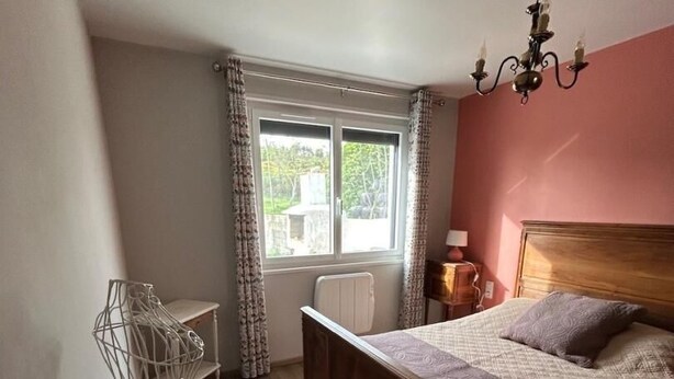 Un dormitorio con cama de madera, una ventana con cortinas, un radiador y una lámpara de araña.