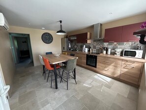 A modern kitchen with a dining area, featuring a wooden table, chairs, and a microwave. - Le Chaumet - SAINT-DENIS-EN-MARGERIDE (SAINT-DENIS-EN-MARGERIDE)