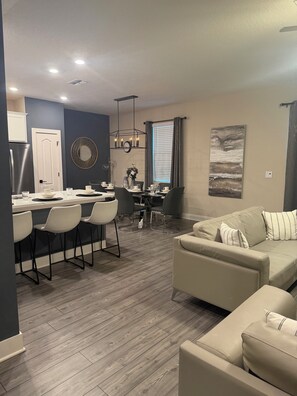 A modern living room with a beige sofa, a dining area with a white table and chairs, and a kitchen with a refrigerator and cabinets. - Perfect 4-bedroom home in Reunion Village West Kissimmee (Kissimmee)