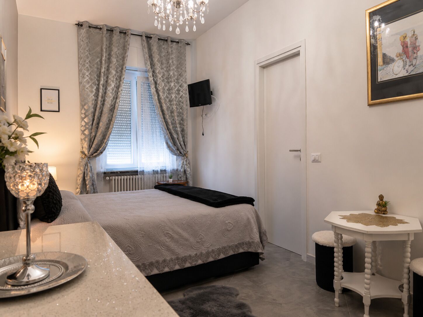 A bedroom with a bed, a television, a small table, and a window with curtains.