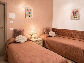 Una camera d'albergo con due letti, un comodino con una lampada e due quadri appesi al muro.