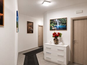 Ein Korridor mit weißer Wand, einer Holztür, einem weißen Schrank mit Schubladen und einem Bild von einem Wasserfall.