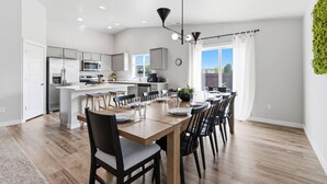 A modern kitchen with white cabinets, a dining area with a wooden table and chairs, and a view of the outdoors. - Curated Comfort in the Treasure Valley (Boise)