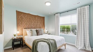 A bedroom with a bed, bedside tables, a window with curtains, and a view of greenery outside. - Curated Comfort in the Treasure Valley (Boise)