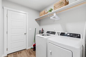A laundry room with two front-loading washers and dryers, a broom, and a mop. - Curated Comfort in the Treasure Valley (Boise)