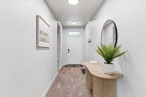 A hallway with a white door, a framed picture on the wall, a potted plant, and a light fixture. - Curated Comfort in the Treasure Valley (Boise)