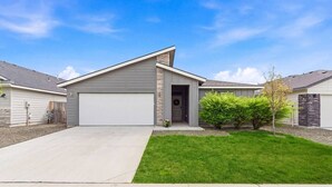 A modern single-story house with a garage, a well-maintained lawn, and a small tree in the front yard. - Curated Comfort in the Treasure Valley (Boise)