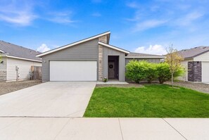 Ein modernes, eingeschossiges Haus mit Garage, einem gepflegten Rasen und einem kleinen Baum im Vorgarten.