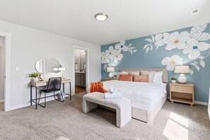 A bedroom with a bed, a desk, a chair, a bench, and a wall with a floral mural. - Curated Comfort in the Treasure Valley (Boise)