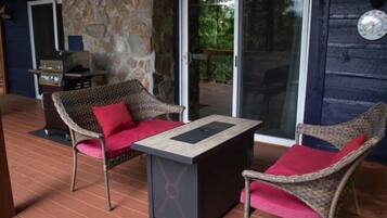 Un espace extérieur aménagé avec des meubles de jardin en osier, une table, un mur en pierre et une porte vitrée donnant sur un patio.