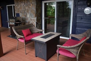 A covered outdoor seating area with wicker chairs and a table, a stone wall, and a glass door leading to a patio.