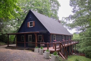 A wooden cabin with a porch, surrounded by trees.