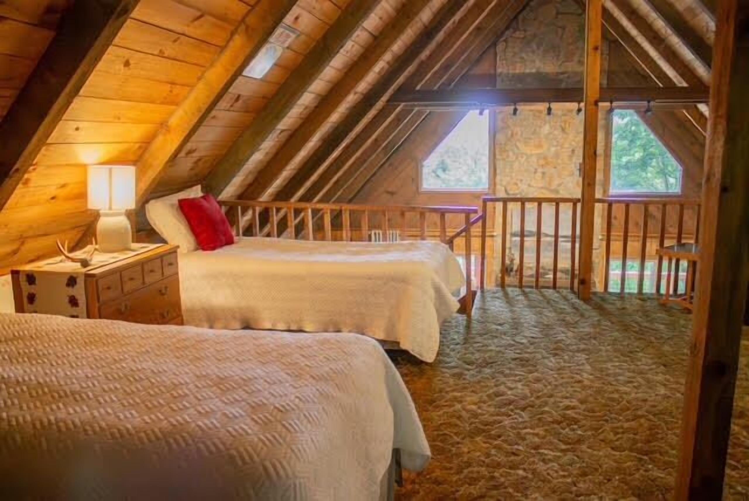 Une chambre mansardée chaleureuse, avec deux lits, un plafond en bois et une vue sur l’extérieur.