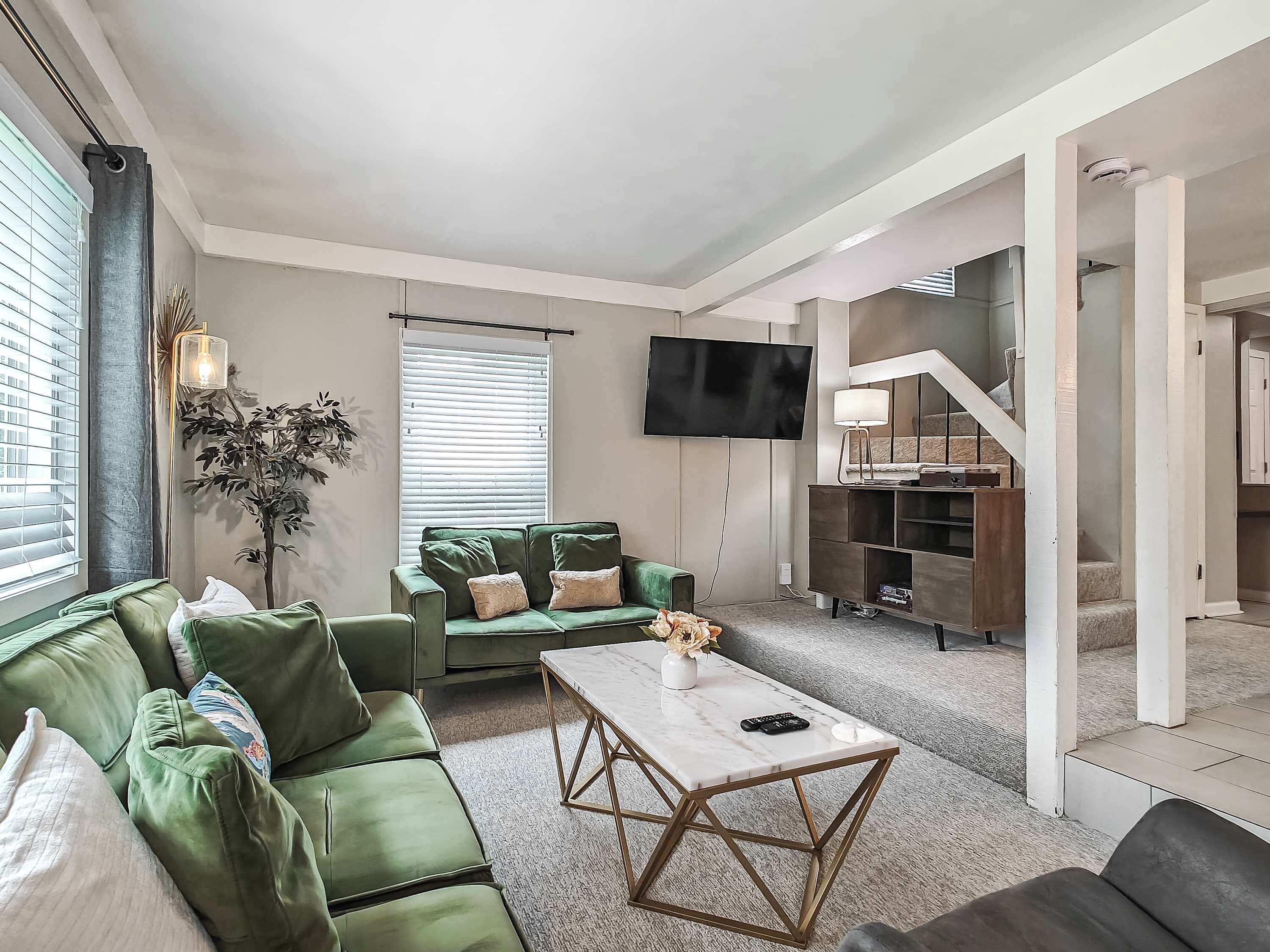 A modern living room with a green sofa, a coffee table, and a TV mounted on the wall.