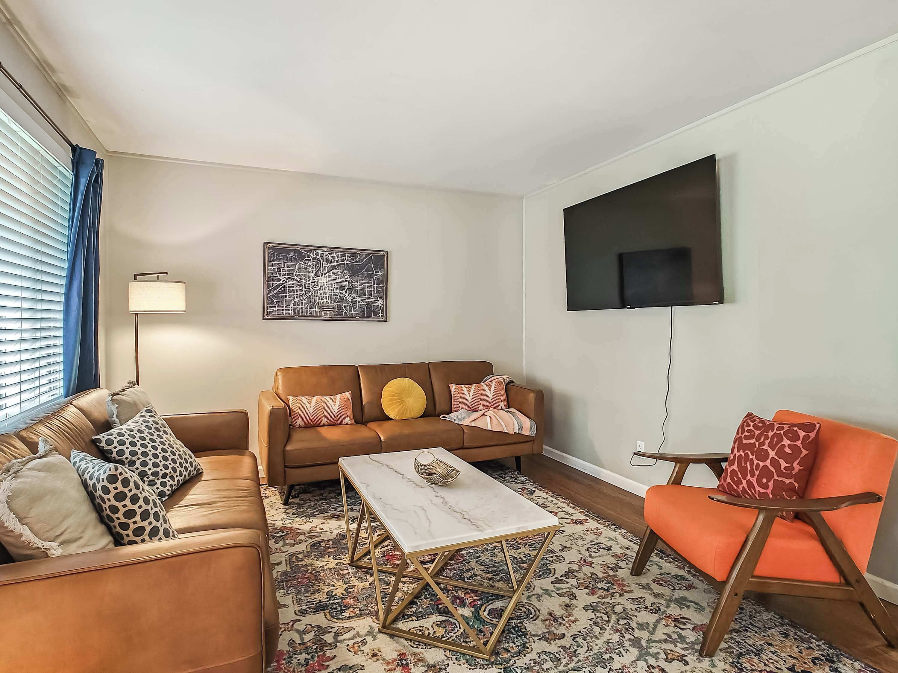 Uma sala de estar com sofá, poltrona, mesa de centro e uma TV de tela plana fixada na parede.
