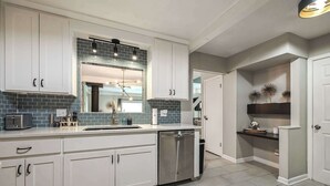 A modern kitchen with white cabinets, a stainless steel dishwasher, and a tiled backsplash. - 4 Bdrm Getaway with Hot Tub (Overland Park)