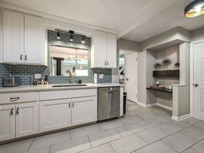 Una cocina moderna con armarios blancos, lavavajillas de acero inoxidable y salpicadero de azulejos.