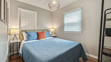 A bedroom with a bed, bedside lamps, a window with blinds, a ceiling light fixture, and a door.