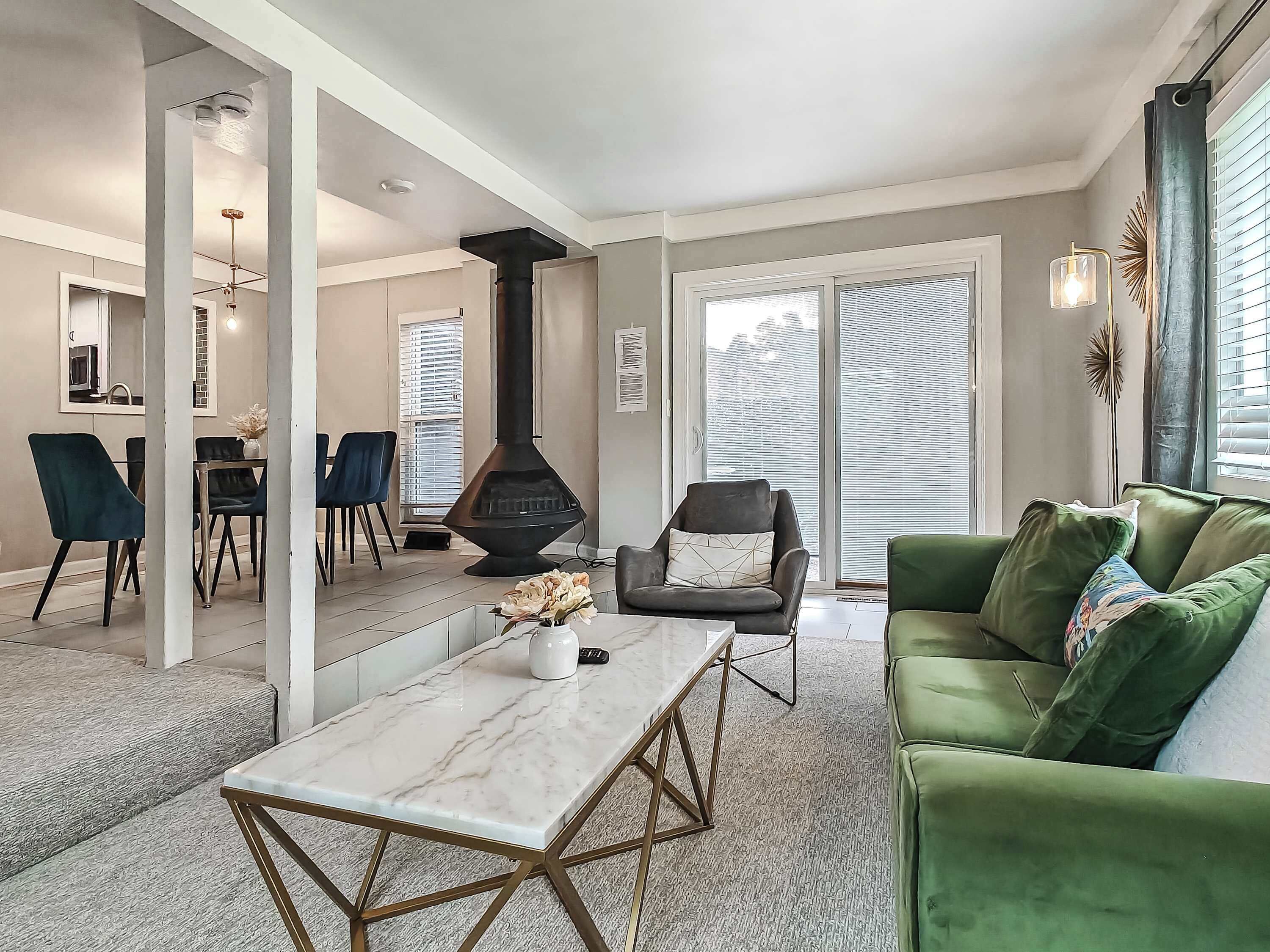 A modern living room with a fireplace, green sofa, and a dining area with chairs.